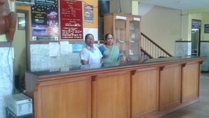 Un mostrador de recepción con acabado de madera y una partición de vidrio. Detrás del mostrador, se observan carteles y una escalera que conduce a un nivel superior.