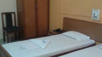Una habitación de hotel con una cama individual, una mesita de noche con teléfono, un armario de madera y una silla.