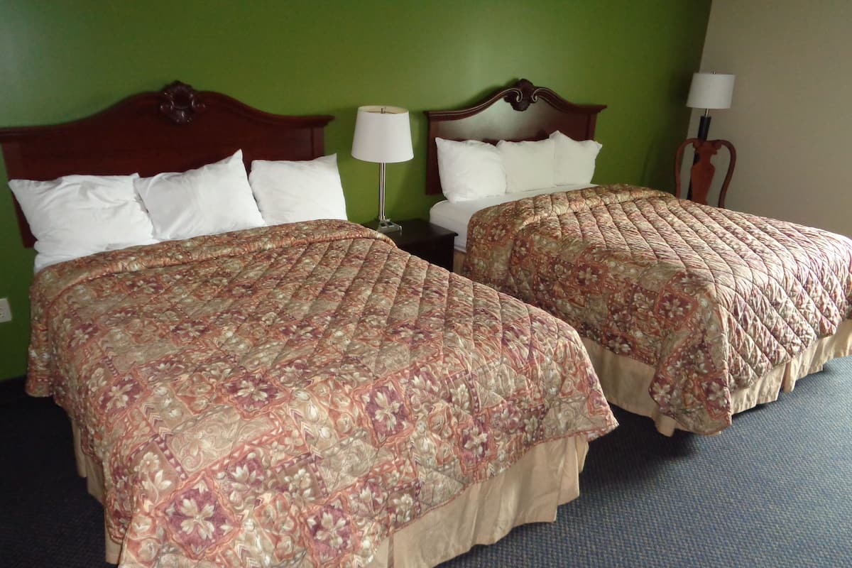 Two double beds with floral bedspreads, a nightstand with a lamp, and green walls.