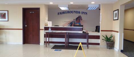 Un espace d’accueil avec une enseigne indiquant « Fairgrounds Inn », un comptoir de réception, une plante en pot et un panneau d’avertissement jaune placé sur le sol.