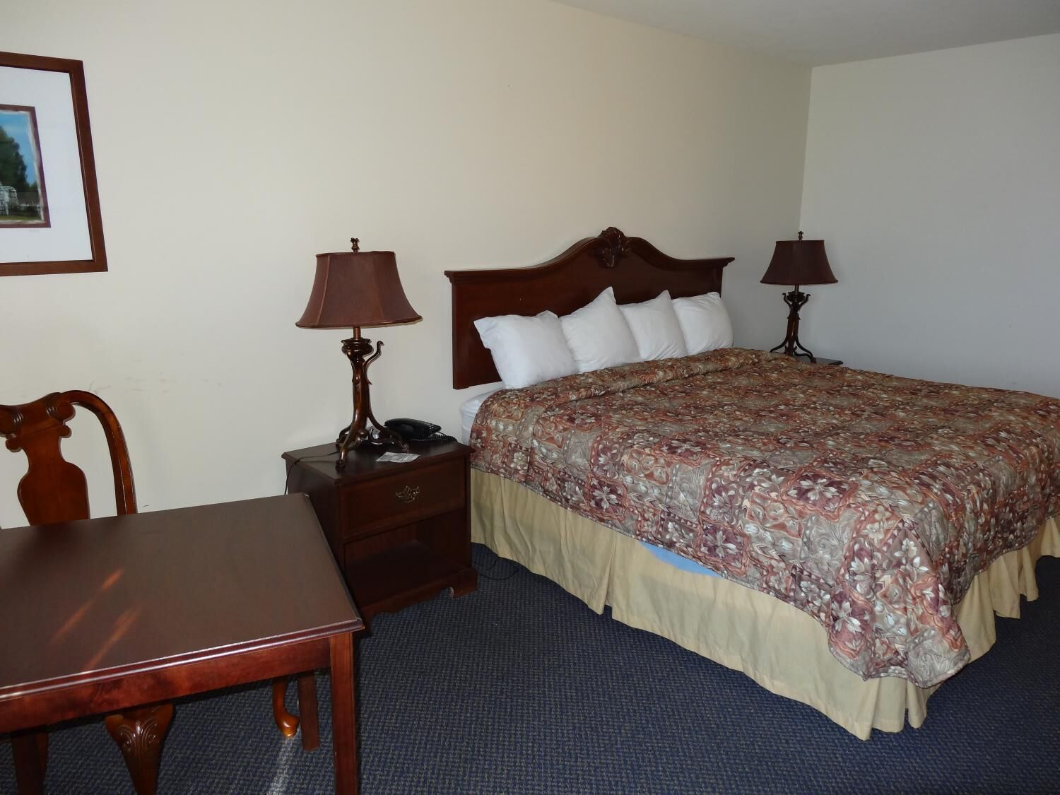 A hotel room with a wooden bed, two bedside tables with lamps, a wooden chair, and a small desk.