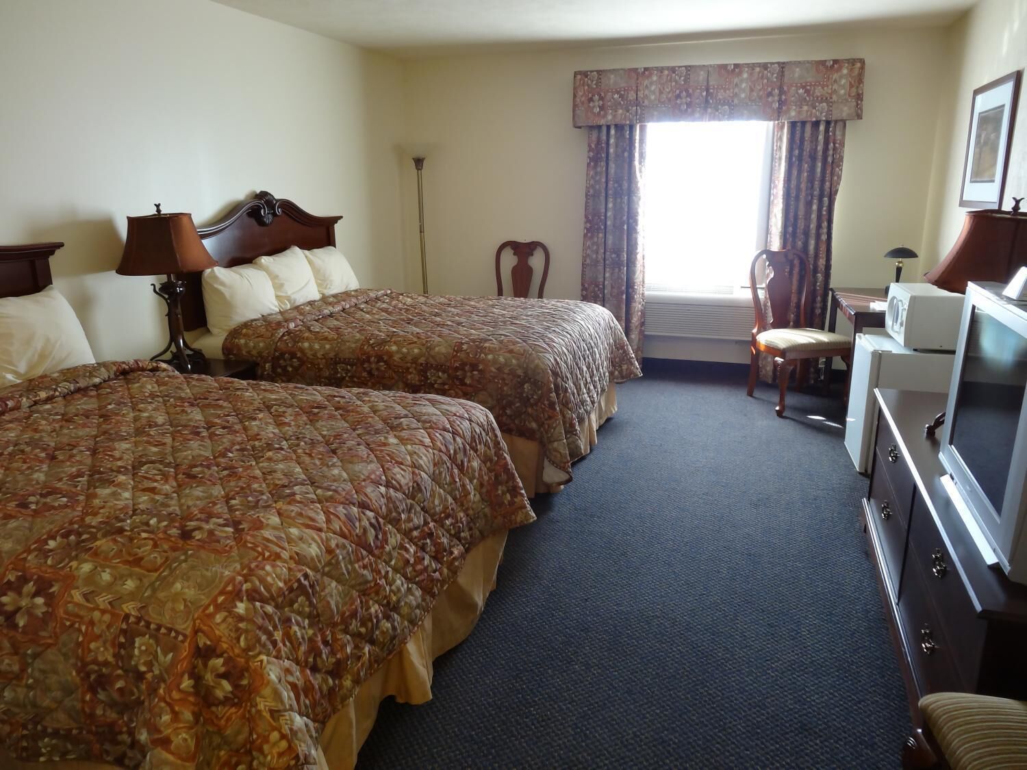 A hotel room with two beds, a desk, a chair, a television, and a window with curtains.