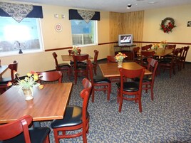 A dining area with wooden tables and chairs, a television on a stand, and a window with a view of the outside.