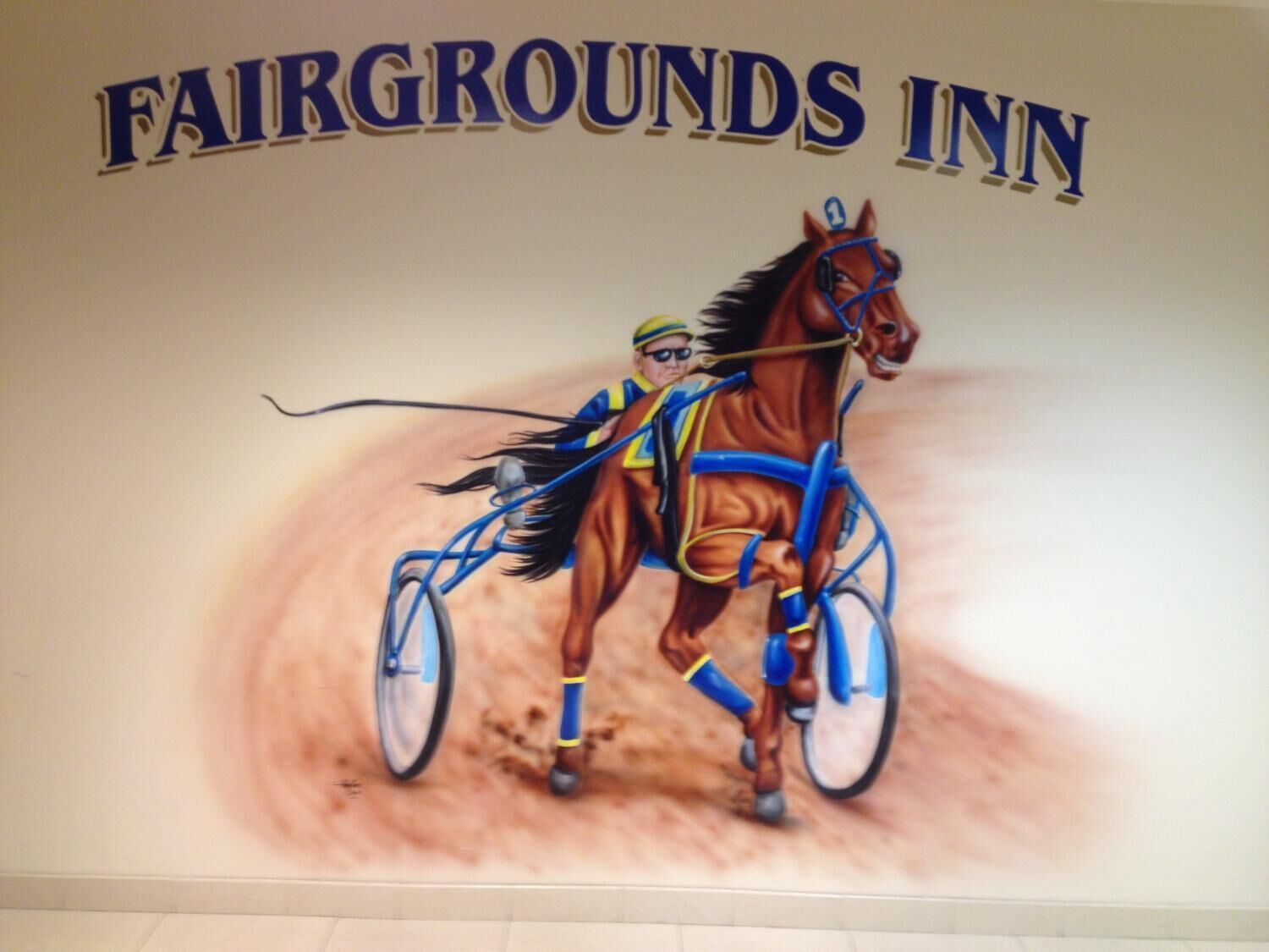 Et mural af en hest og rytter på en hestevogn, med teksten "FAIRGROUNDS INN" over.
