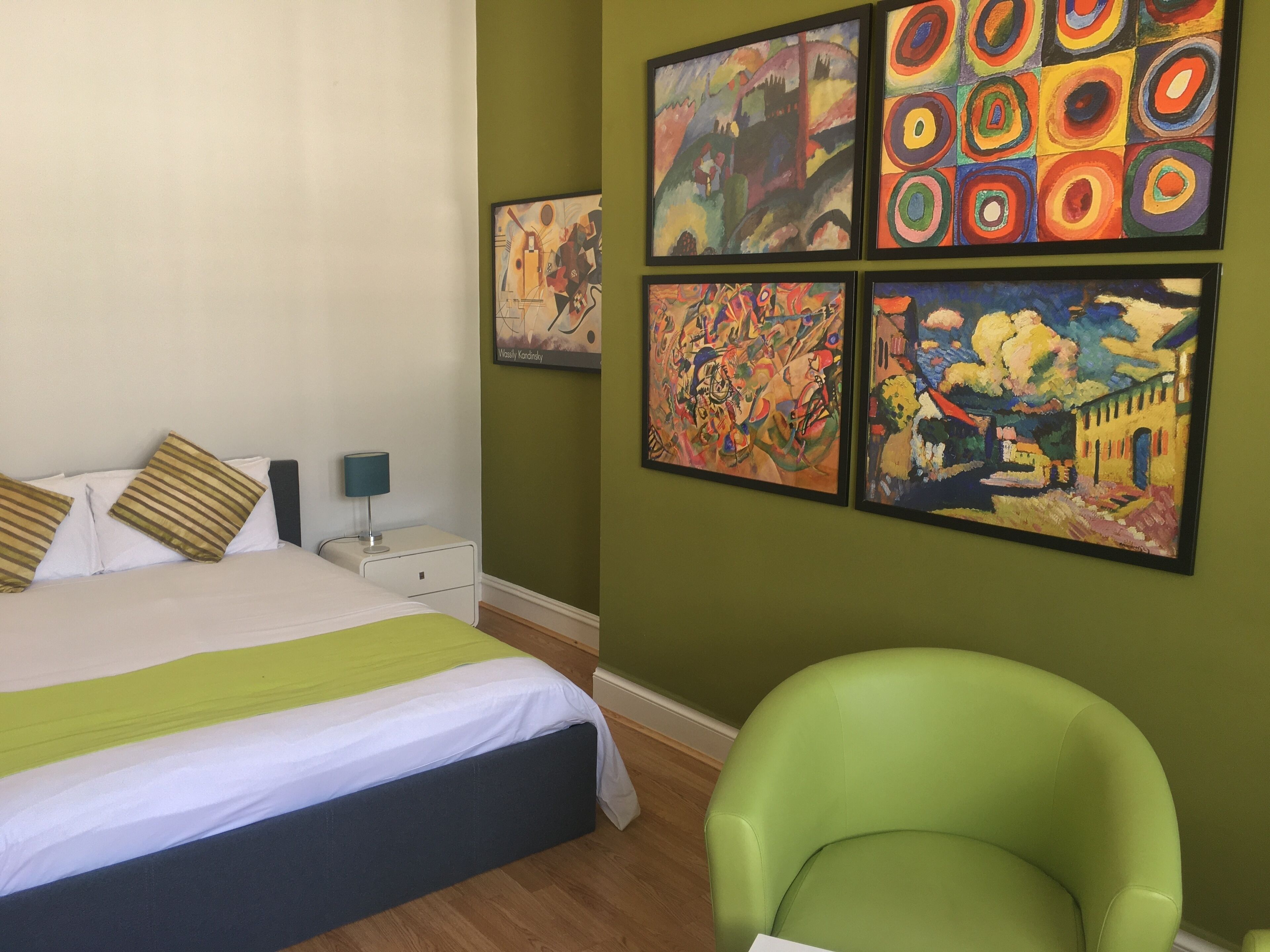 Un dormitorio con una cama, paredes verdes y cuatro cuadros.
