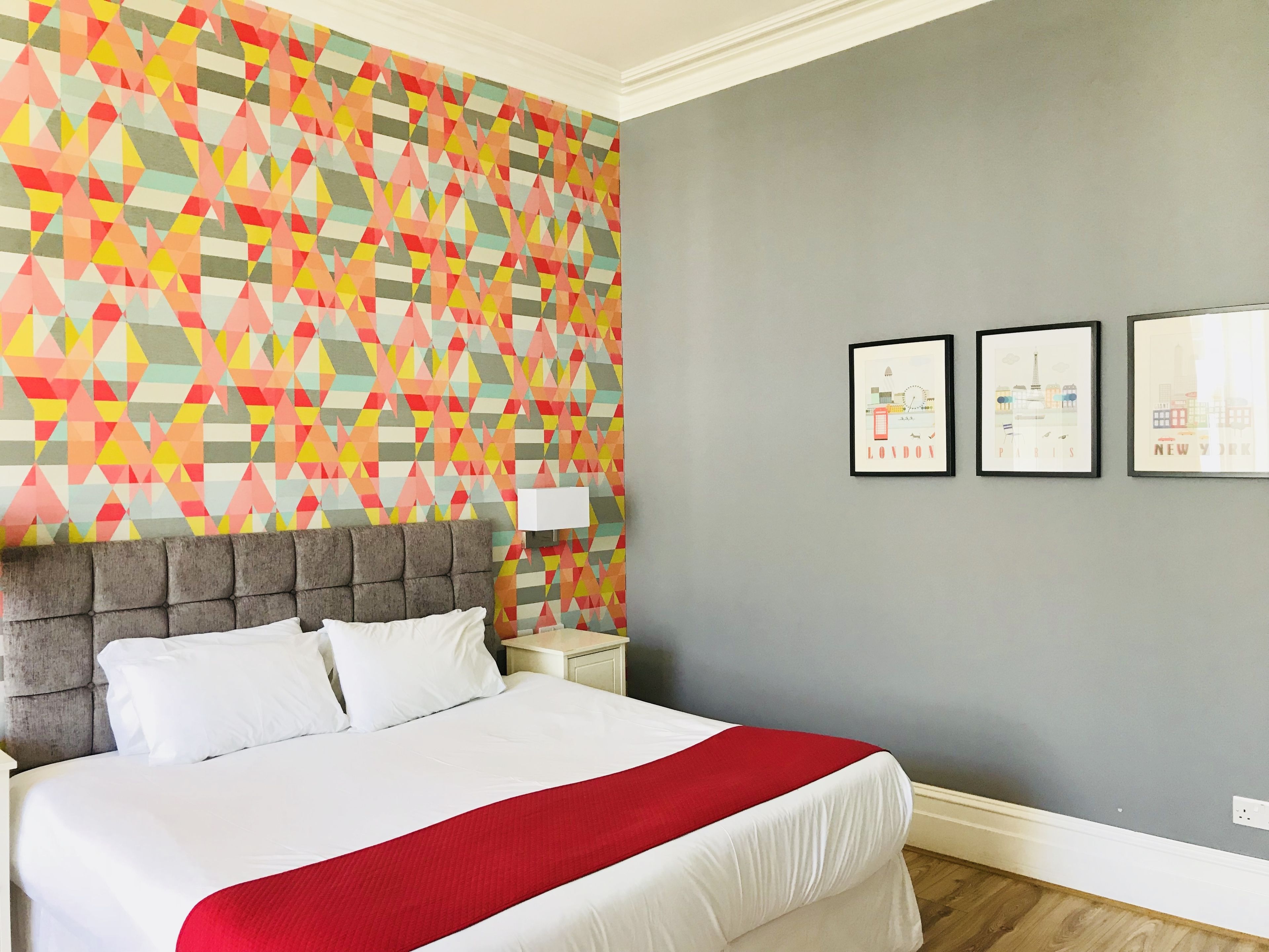 A hotel room with a bed, a geometric-patterned wall, and three framed pictures on the wall.