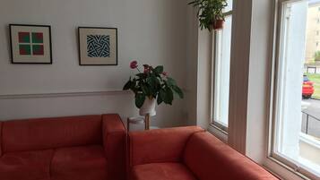 A room with two red sofas, a potted plant with red flowers, and two framed artworks on the wall.