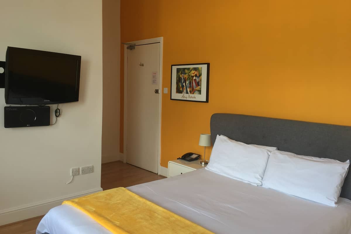 A hotel room with a bed, a TV, a bedside table with a lamp, and a door.