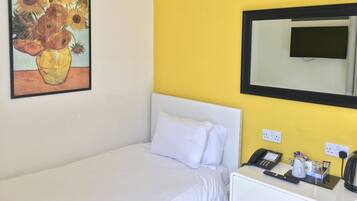 A hotel room with a bed, a bedside table with a phone and a coffee maker, a painting of sunflowers, and a mirror on the wall.