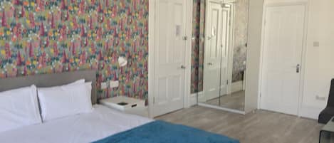 Un dormitorio con cama, mesita de noche, espejo y puerta.