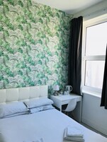 Una habitación de hotel con cama, escritorio con lámpara, cafetera y ventana con cortinas.
