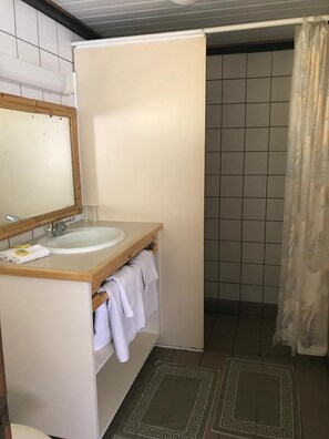 A bathroom with a wooden vanity, a sink, a mirror, and a shower area with a curtain. - Pension Motu Iti (Moorea-Maiao)