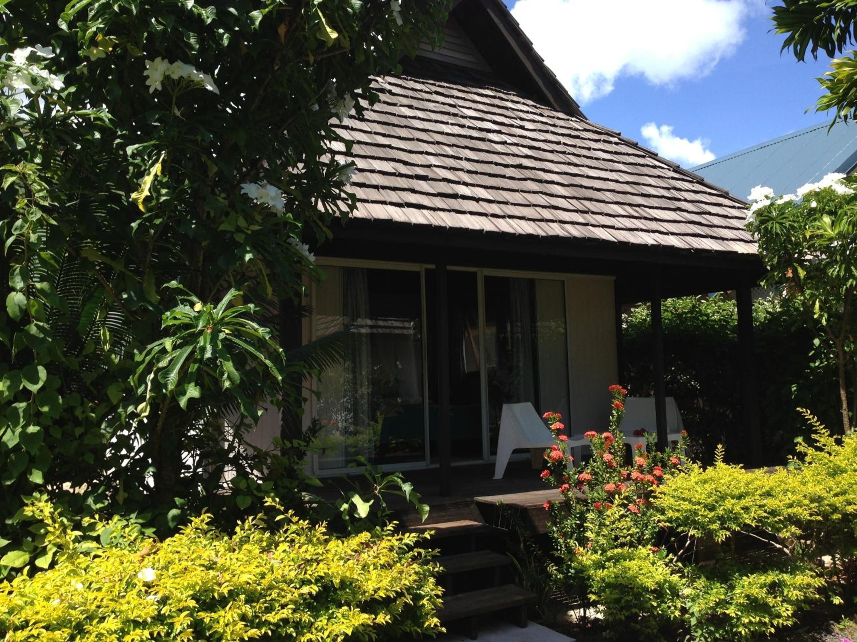 A house with a sloped roof, a covered porch, and a garden with various plants and flowers.