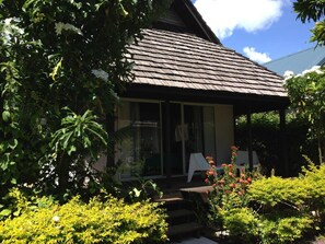 A house with a sloped roof, a covered porch, and a garden with various plants and flowers. - Pension Motu Iti (Moorea-Maiao)