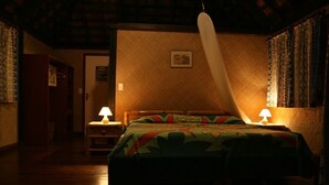 Um quarto com iluminação fraca, com uma cama, duas luminárias de cabeceira, um guarda-roupa de madeira e um papel de parede estampado.