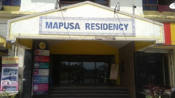The entrance to Mapusa Residency with a sign above the door, a staircase leading up to the entrance, and a few posters on the wall to the left.