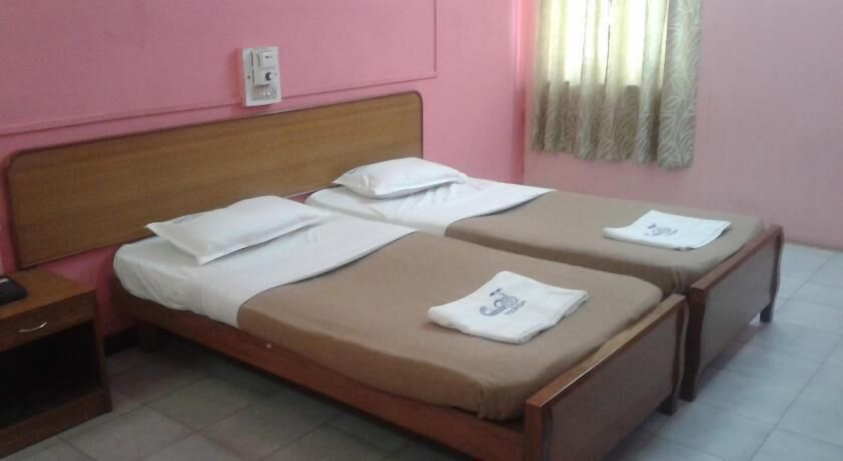 A double bed with a wooden headboard, a bedside table, and a power outlet on the wall.