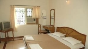 A hotel room with a double bed, a desk with a chair, a television, and a window with curtains.