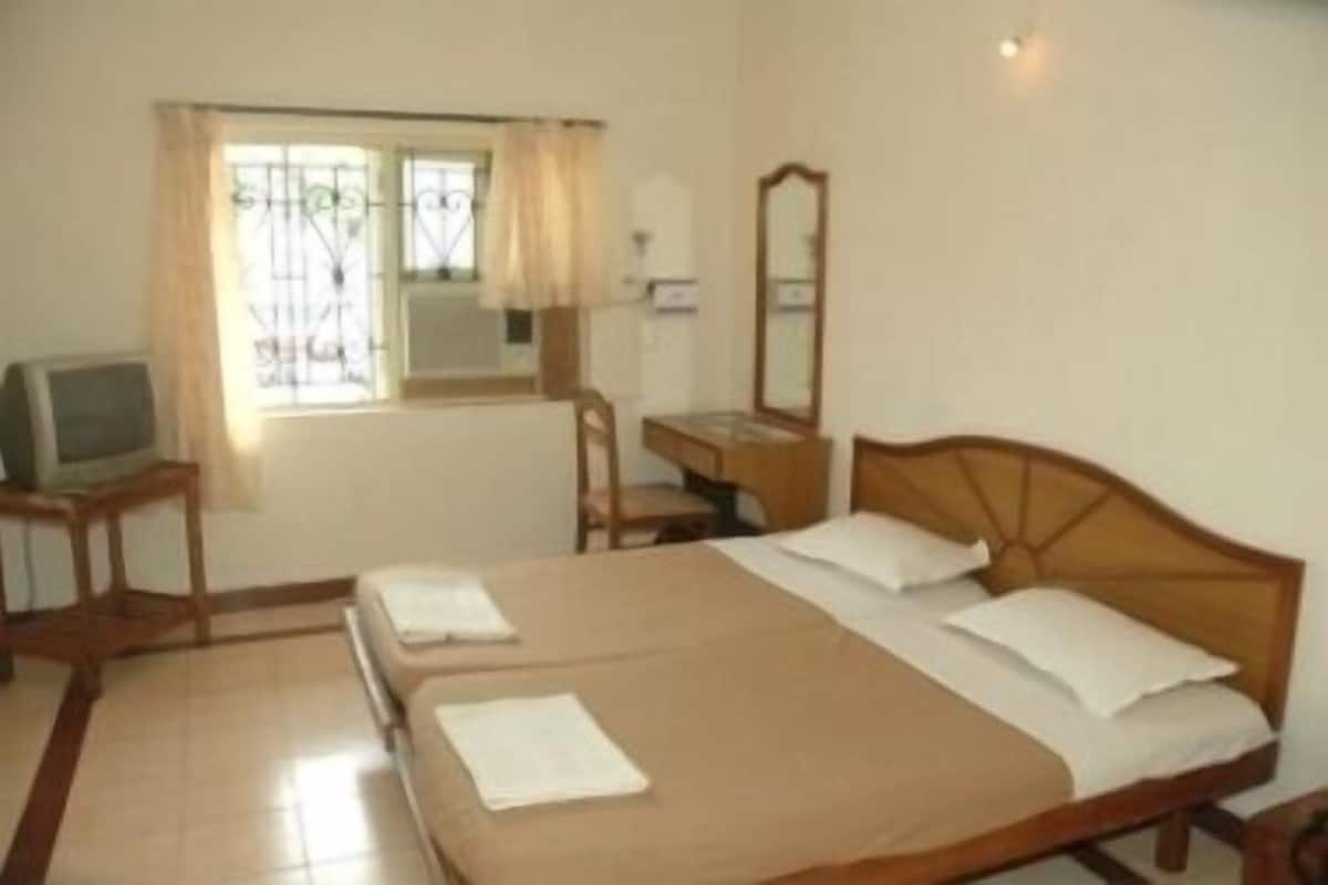 Habitación de hotel con cama doble, escritorio con silla, televisión y ventana con cortinas.