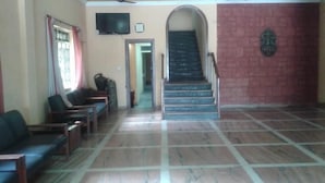 A reception area with a staircase leading to an upper floor, a flat-screen TV mounted on the wall, and a seating area with chairs.