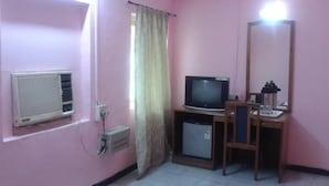 A pink-walled room with a television, a mirror, and a small cabinet.