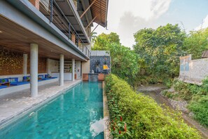 Zona de piscina con muro de piedra, asientos y vistas al verdor.
