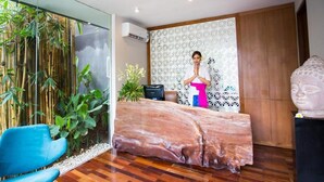 Una habitación con un amplio mostrador de recepción de madera, una silla azul, una pared decorada con bambú y una estatua.