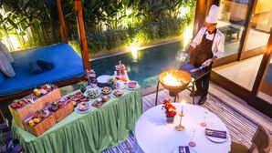 Un área de comedor al aire libre con piscina, un chef preparando comida y una variedad de platos en una mesa buffet.
