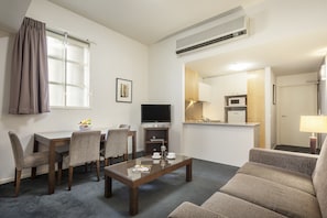 A hotel room with a dining area, a sofa, a TV, and a kitchenette.