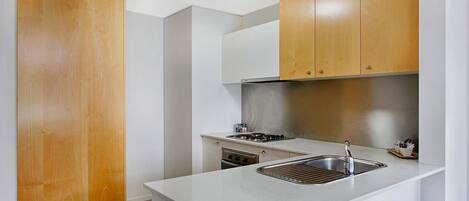 Cocina compacta con un lavamanos de acero inoxidable, una estufa y armarios de madera.