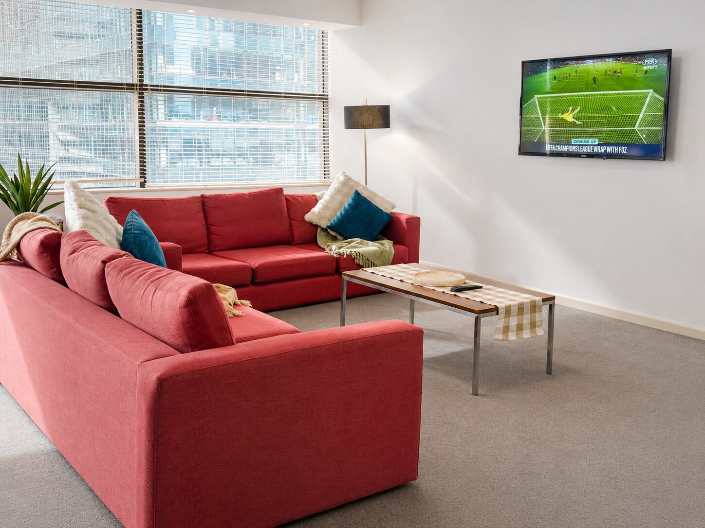 Ein modernes Wohnzimmer mit einem roten Sofa, einem Couchtisch und einem Fernseher, der ein Fußballspiel zeigt.
