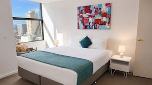 A modern hotel room with a large bed, a city view, a colorful abstract painting, and a nightstand with a lamp.