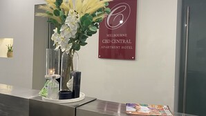 A reception desk with a vase of white flowers, a sign for Melbourne CBD Central Apartment Hotel, and a magazine on the counter.