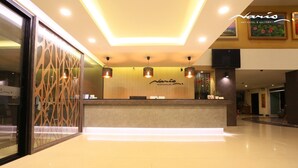 A hotel reception area with a modern design, featuring a reception desk, a wall-mounted sign, and a large vase with flowers. - Naris Art Hotel (Pattaya)