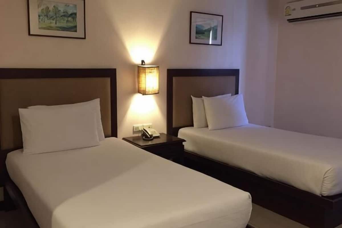 A hotel room with two beds, a nightstand with a lamp, and framed pictures on the wall.