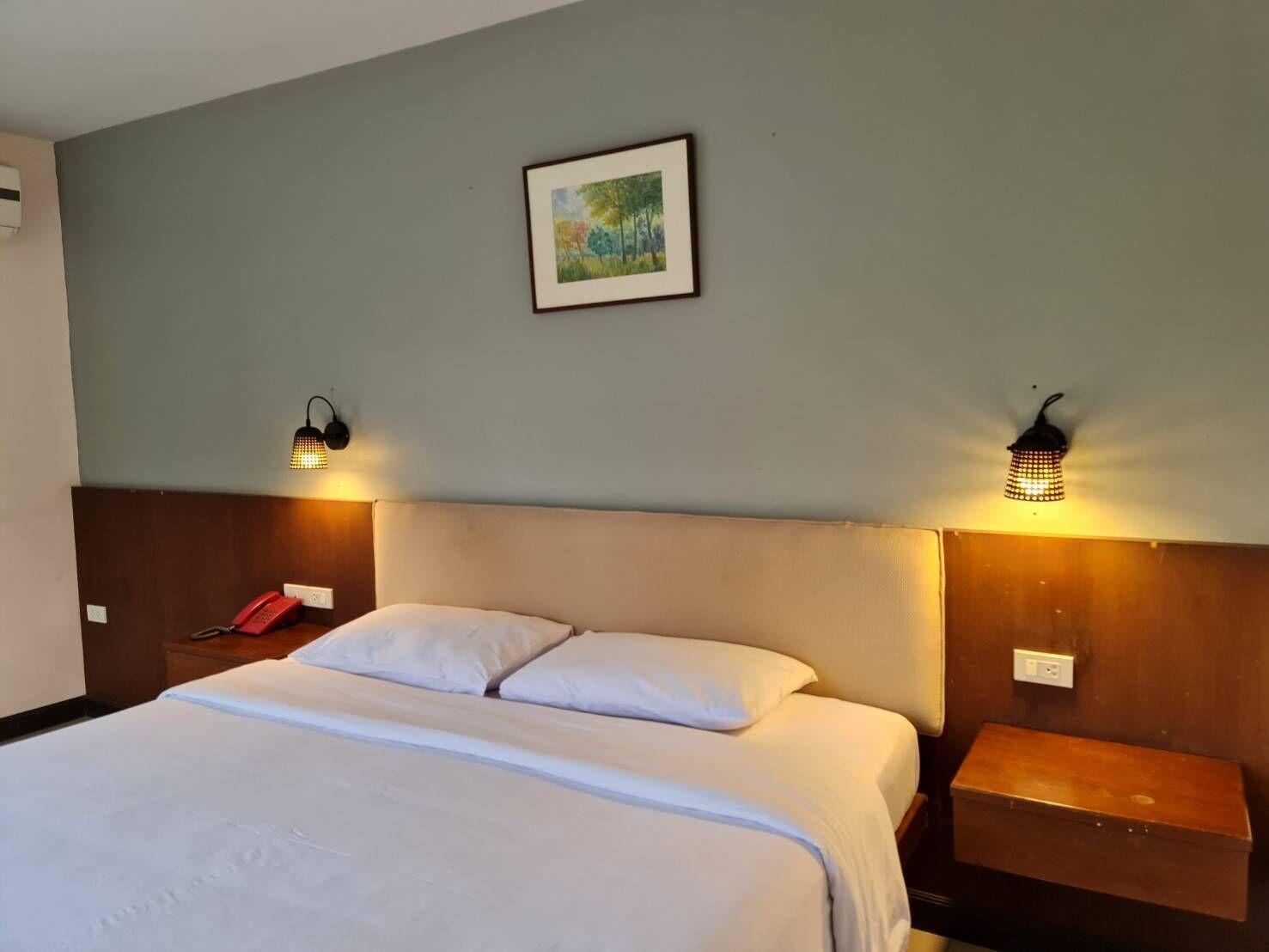 A hotel room with a bed, two bedside lamps, a bedside phone, a nightstand, and a framed picture on the wall.