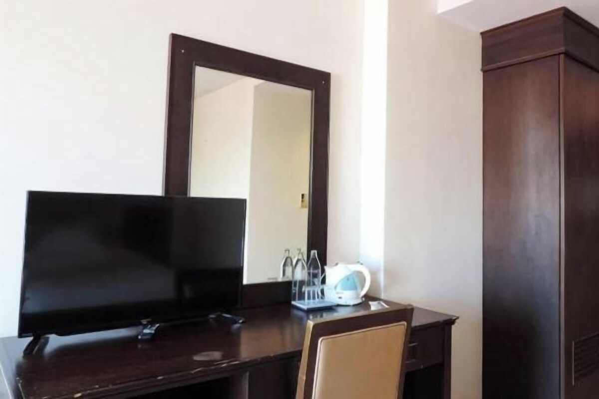 A room with a dark wooden desk, a flat-screen TV, a mirror, and a wardrobe.