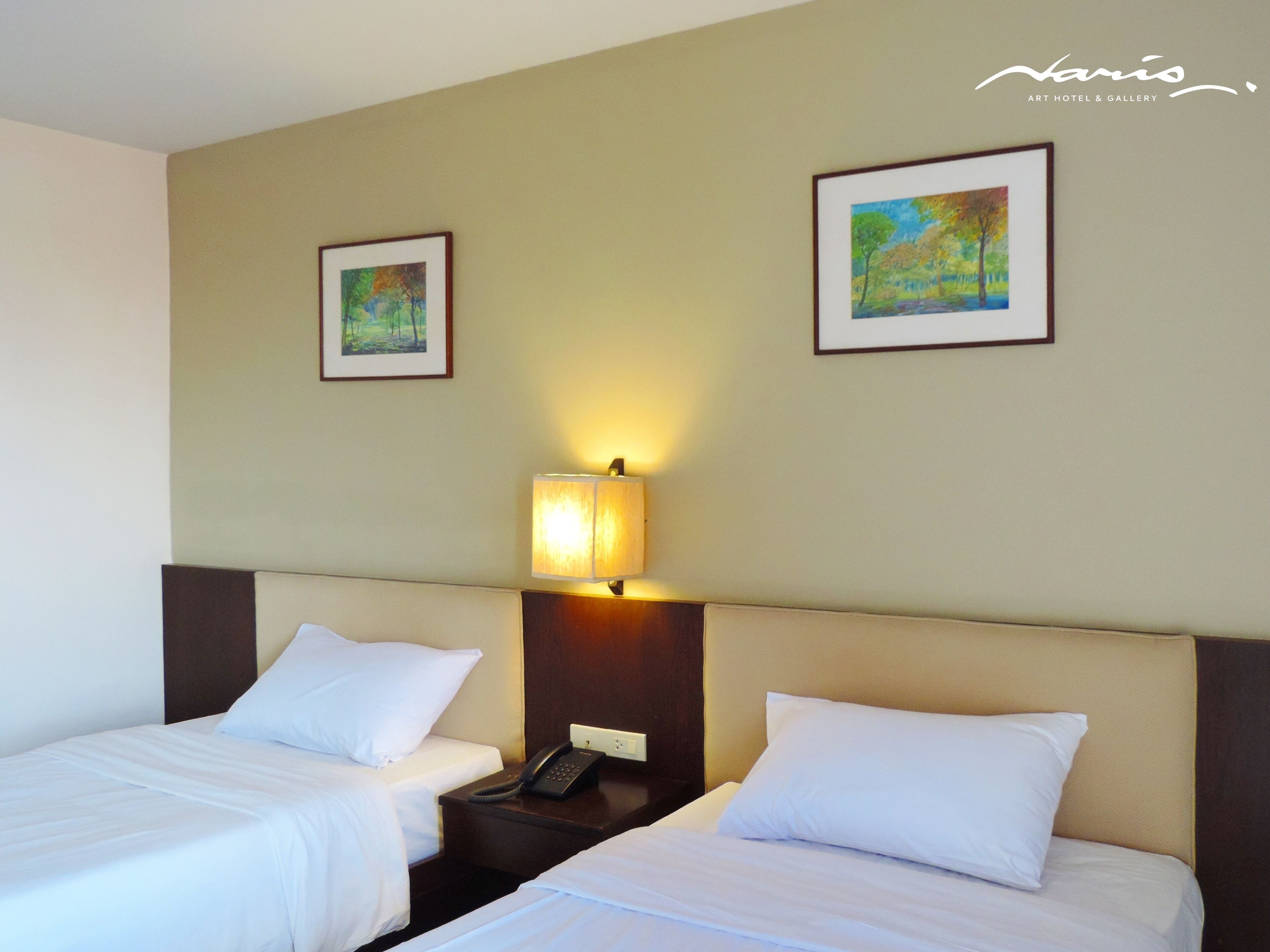 Une chambre d’hôtel avec deux lits, une table de chevet avec une lampe et deux tableaux encadrés au mur.