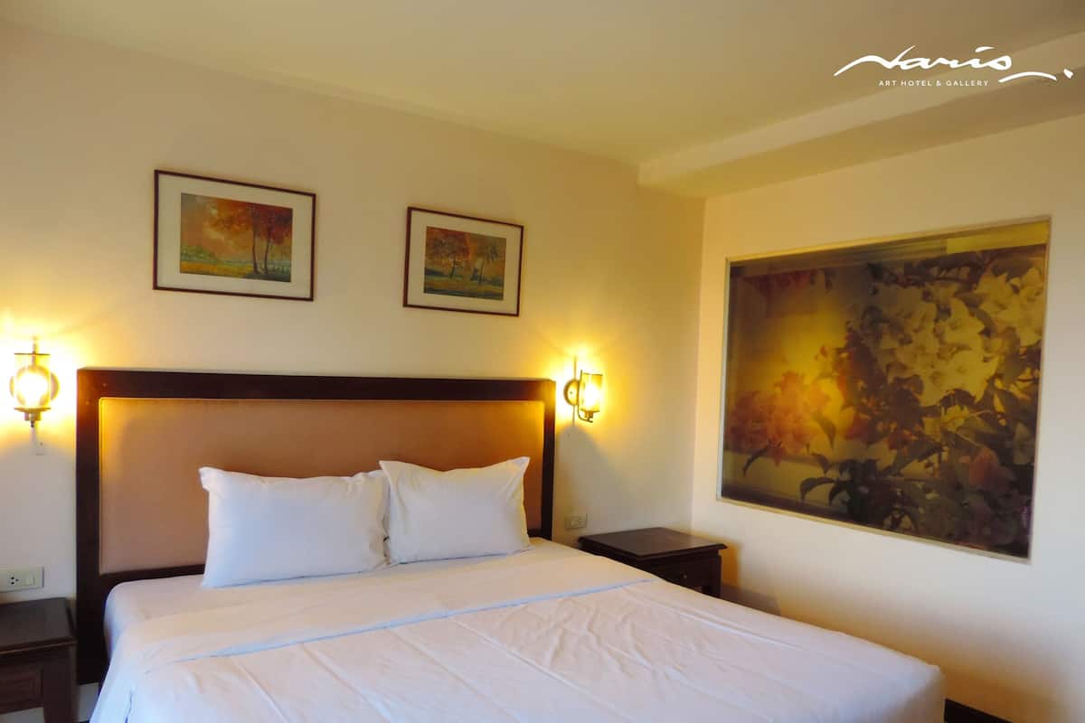 A hotel room with a large bed, two wall-mounted lamps, and two framed pictures above the bed.