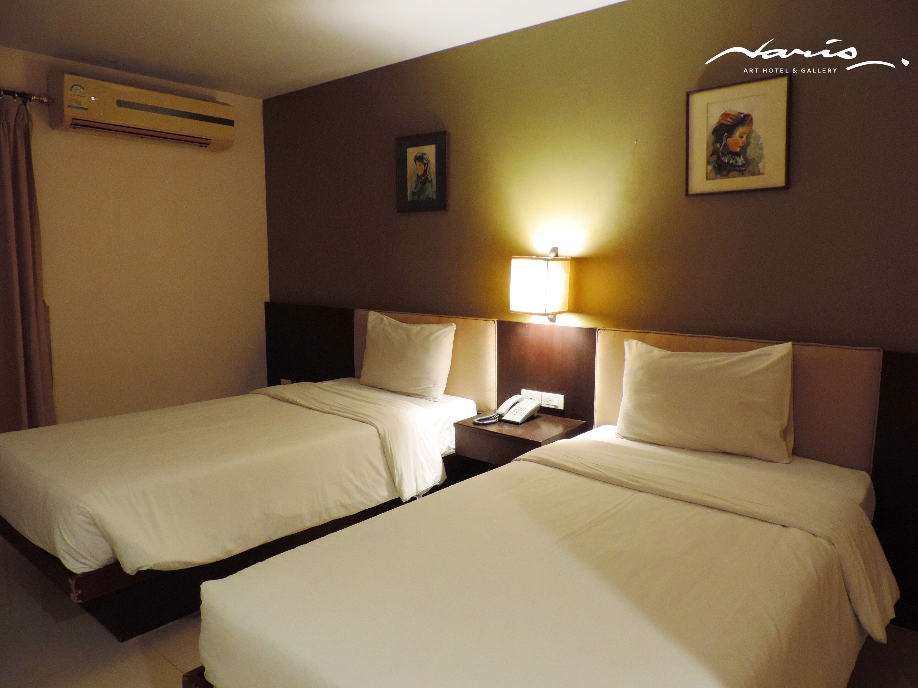A hotel room with two beds, a nightstand with a phone, and a wall-mounted air conditioner.