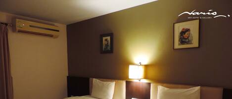 A hotel room with two beds, a nightstand with a phone, and a wall-mounted air conditioner.