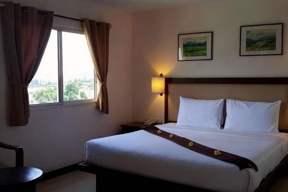 A hotel room with a large bed, a bedside table, a window with curtains, and two framed pictures on the wall.