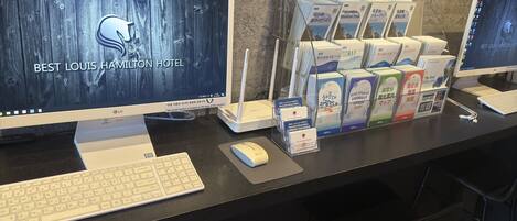 A hotel reception desk with a computer monitor displaying the hotel's name, a keyboard, a mouse, and a set of brochures and maps.