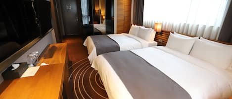 A hotel room with two beds, a desk, a mirror, and a large window with curtains.