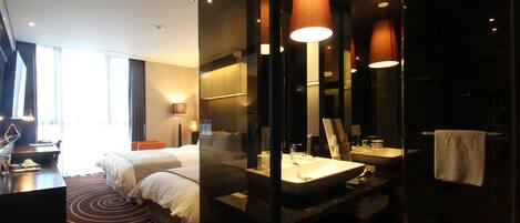 A modern hotel room with a large bed, a desk, a bathroom with a sink and mirror, and large windows.