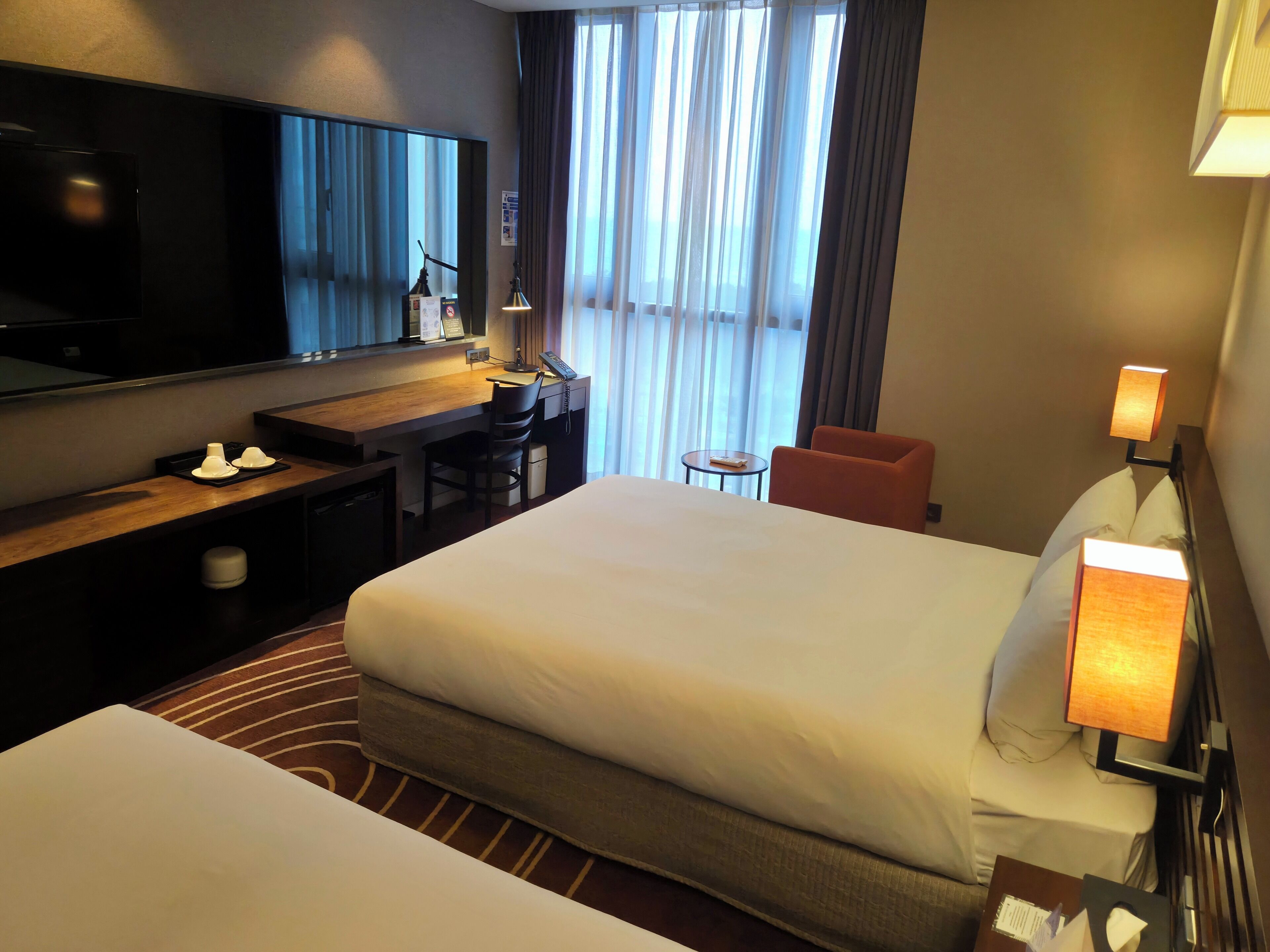 A hotel room with a large bed, a desk with a chair, a television, and a small table.