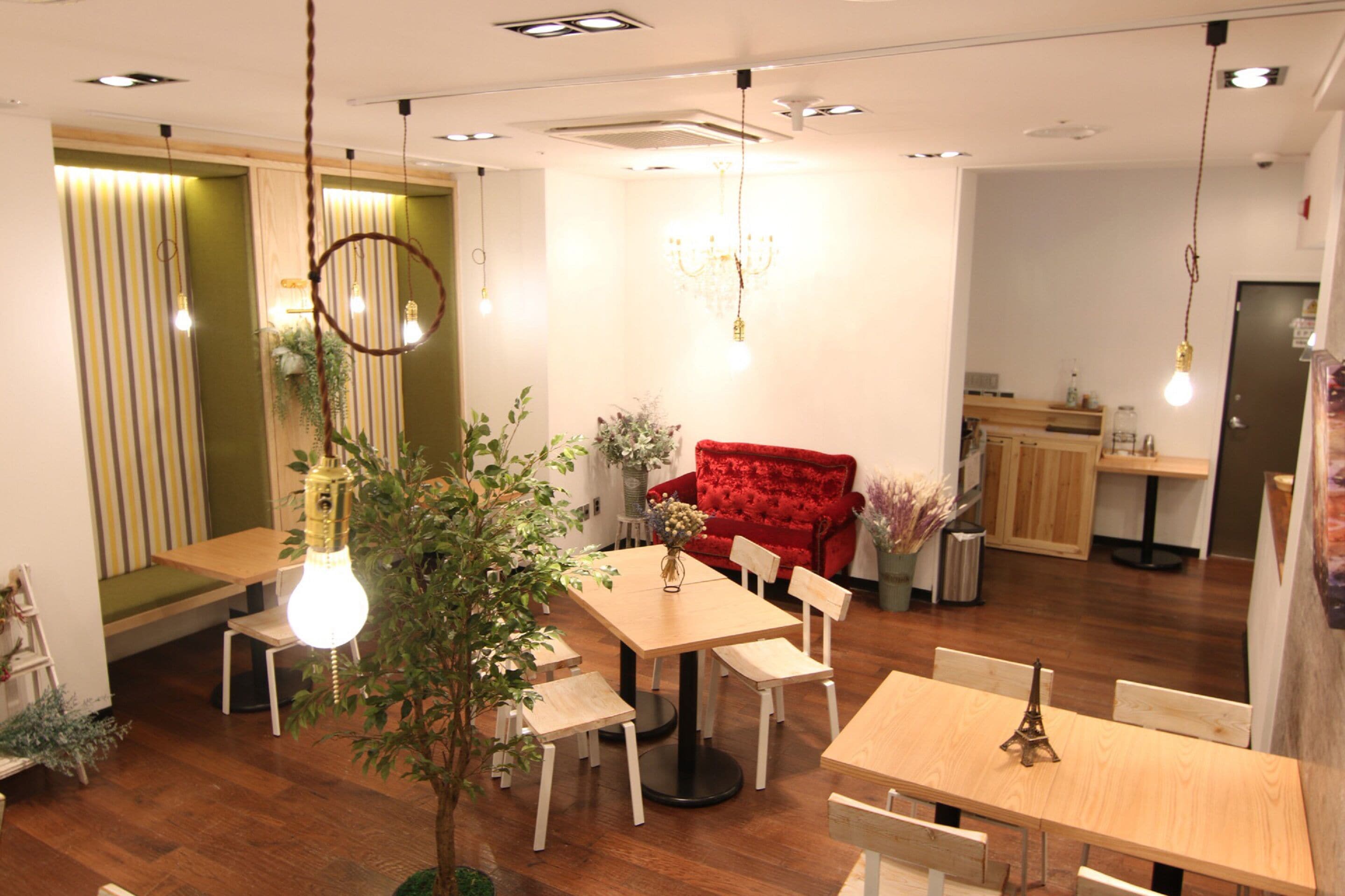 A modern dining area with wooden tables and chairs, a red sofa, and hanging light fixtures.