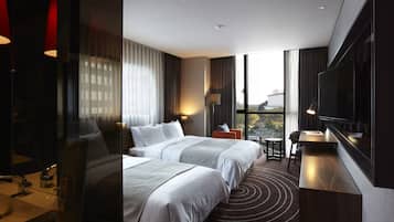 A modern hotel room with two beds, a desk, a TV, and a view of the city.