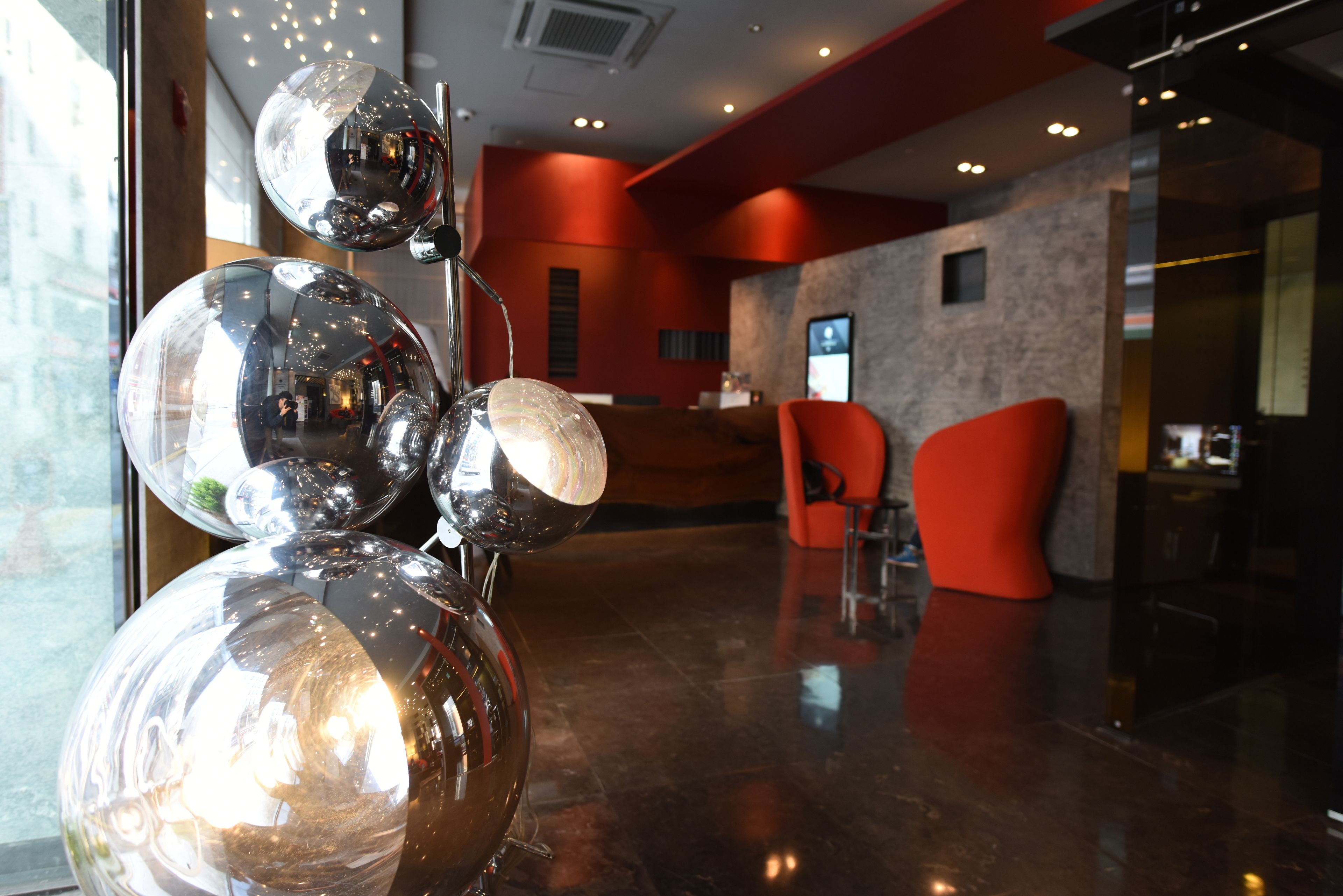 A reception area with a modern design, featuring a glass wall, red accents, and a reflective sculpture.