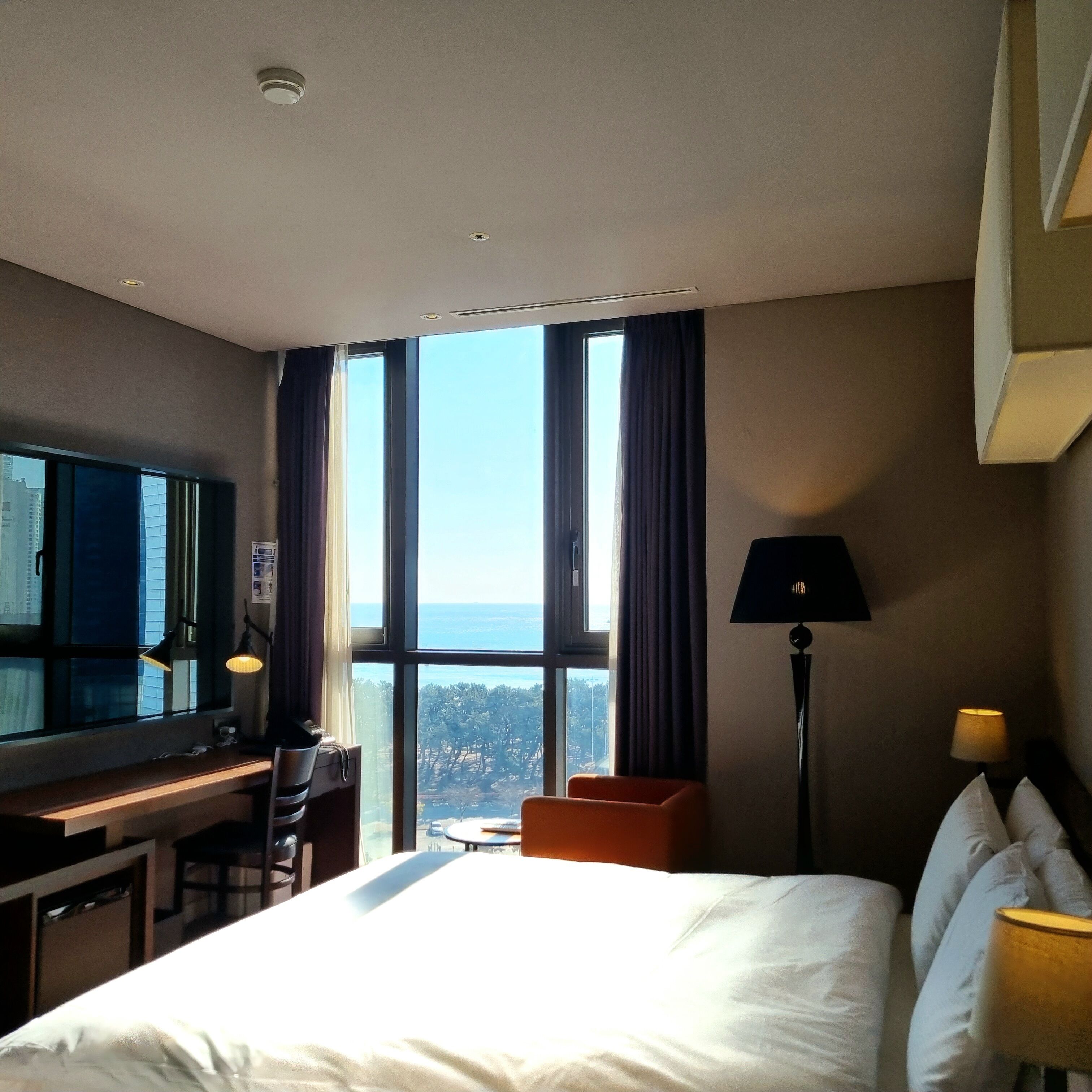 A hotel room with a bed, a desk, a chair, a TV, and a view of the city.